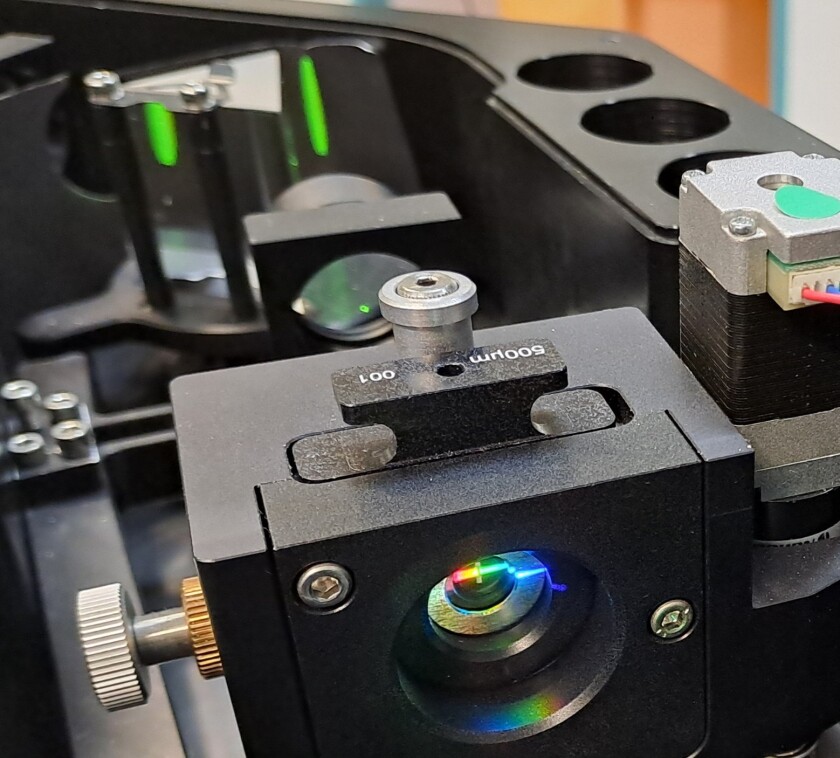 The patented monochromator consists of quartz glass optics with two prisms and a few lenses. The picture shows the central slit, the intermediate lens and the second prism with green reflections in the background.